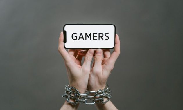 Gambar konseptual seseorang yang memegang smartphone bertanda 'GAMERS' dengan tangan terantai / pexels-tima-miroshnichenko